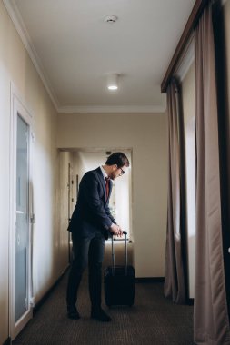 Bir otel koridorunda bavulla yürüyen bir iş adamı.