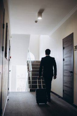 Bir otel koridorunda bavulla yürüyen bir iş adamı.