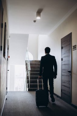 Bir otel koridorunda bavulla yürüyen bir iş adamı.