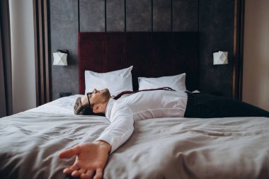 Yorgun iş adamı uzun bir uçuş sonrası yatakta dinleniyor, jet lag. Takım elbiseli bir adam otel odasındaki şilteye uzanmış yatıyordu..
