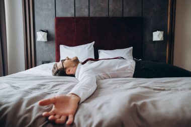 Yorgun iş adamı uzun bir uçuş sonrası yatakta dinleniyor, jet lag. Takım elbiseli bir adam otel odasındaki şilteye uzanmış yatıyordu..