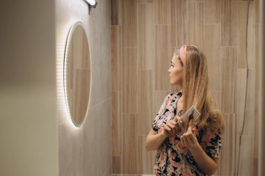 Sarışın kız aynanın önünde saçlarını tarıyor.