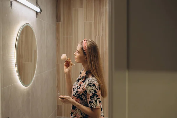 stock image Blonde girl doing makeup on in front of the mirror