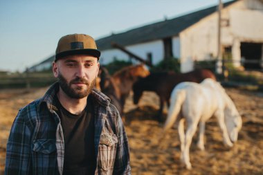 Çiftlikteki at sürüsünün yanında genç bir çiftçi. Gün batımında at sırtında sakallı bir gencin portresi..