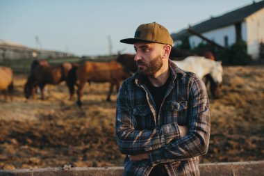 Genç bir çiftlik işçisinin portresi, arka planda atlarla birlikte. Genç bir çiftçi ahırda atlara bakar..