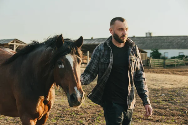 若い農夫は馬と一緒にパドックで働いている 若い男が農場で馬の世話をする — ストック写真