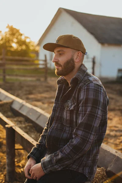 Portrait of a handsome young man in a cap near the fence of a rural ranch.
