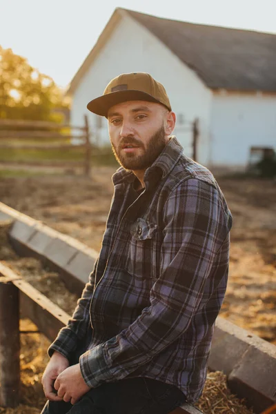Portrait of a handsome young man in a cap near the fence of a rural ranch.
