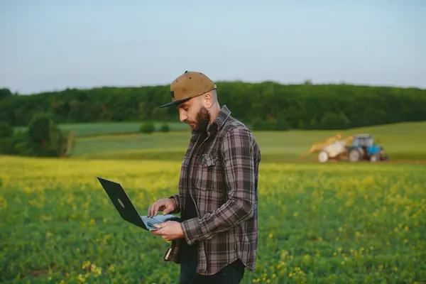Rolnik Sprawdza Pracę Terenie Człowiek Laptopem Monitoruje Pracę Ciągnika Terenie — Zdjęcie stockowe