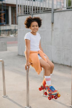 Patenli Afro-Amerikalı genç kız dışarıda eğleniyor. Kız kameraya bakarak gülümsüyor..