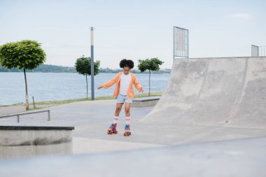 Yaz parkında paten kayan tatlı Afrikalı Amerikalı küçük kız. Çocuk parkta eğleniyor, komik küçük kız yolda paten kayıyor. spor öğrenme konsepti