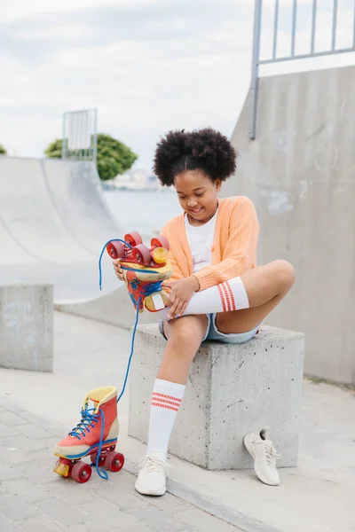 Stock image A teenage girl takes off her roller skates after skating. African American girl having fun at the skatepark on the weekend.