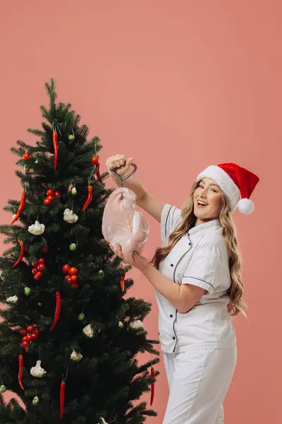 料理とクリスマス休暇のコンセプト サンタの帽子で美しいブロンドの料理は クリスマスツリーの背景に対してポーズ — ストック写真