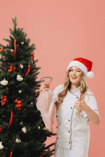 料理とクリスマス休暇のコンセプト サンタの帽子で美しいブロンドの料理は クリスマスツリーの背景に対してポーズ — ストック写真