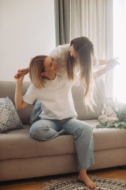 Anne kucağında küçük tatlı kızı kanepede oturmuş evde eğlenceli bir oyun zamanı geçiriyor..