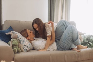 Sevimli küçük kız kucaklaşması heyecanlı genç anne sevgi ve şefkat göster, gülümseyen anne ve komik küçük kız evde eğlenin..