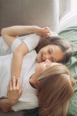 Anneler Günü. Bir anne ve kızı oynuyorlar, gülümsüyorlar ve sarılıyorlar. Anne ve kızı izin gününde evdeki kanepede..