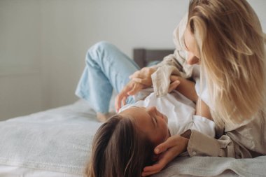 Mutlu anne-kız eğleniyor ve evde yatakta birlikte oynuyorlar..