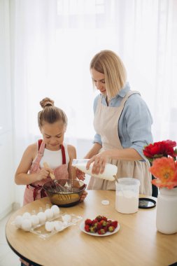 Anne ve kızı modern bir mutfakta masada krep hamuru hazırlıyorlar. Kız çırpıcıyı tutuyor, yumurtayı bir kasede karıştırıyor, annesiyle hamuru hazırlıyor..