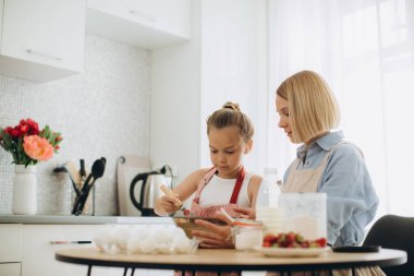 Anne ve kızı modern bir mutfakta masada krep hamuru hazırlıyorlar. Kız çırpıcıyı tutuyor, yumurtayı bir kasede karıştırıyor, annesiyle hamuru hazırlıyor..