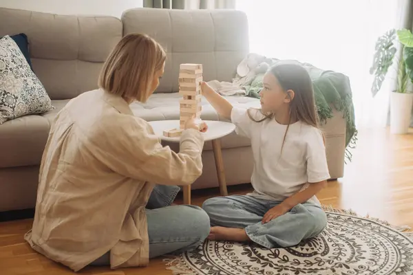 Family plays board game. Cheerful and friendly young woman and her daughter are having fun playing Jenga together. Family spending time together at home on day off.