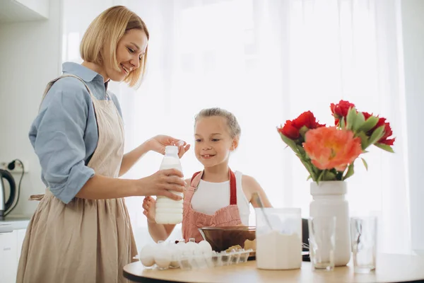 A young beautiful mother teaches her little daughter how to make pancake batter. Mother and daughter in the kitchen together.