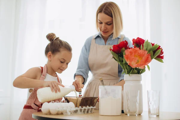 A young beautiful mother teaches her little daughter how to make pancake batter. Mother and daughter in the kitchen together.