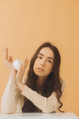 Bir kavanoz nemlendirici kremi olan güzel bir kadın. Bej arka planda mükemmel ciltli bir kadının fotoğrafı. Güzellik ve Cilt Bakımı.