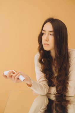 Güzel esmer kadın elinde tonal kapatıcı, bej arka planda izole edilmiş..