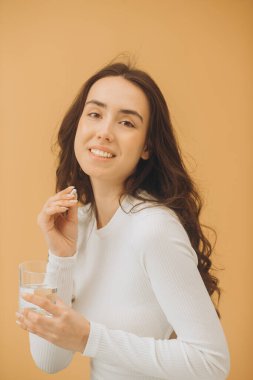 Vitamin alan genç ve güzel bir kadın. Bir kadın elinde bir hap ve bir bardak su tutuyor..