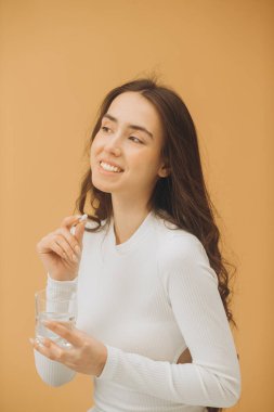 Vitamin alan genç ve güzel bir kadın. Bir kadın elinde bir hap ve bir bardak su tutuyor..