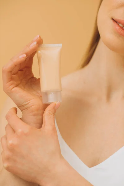 A woman is holding a tube with cosmetic cream. Studio portrait of a pretty woman on a beige background. Close up.