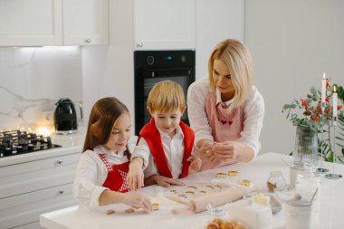 Mutfakta farklı şekillerde kurabiye kesen çocuklu mutlu bir anne. Anne ve kız ve oğlu evde Noel kurabiyesi yapıyorlar ve eğleniyorlar..