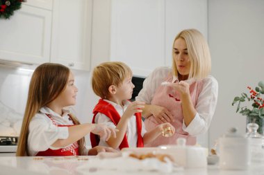 Mutfakta farklı şekillerde kurabiye kesen çocuklu mutlu bir anne. Anne ve kız ve oğlu evde Noel kurabiyesi yapıyorlar ve eğleniyorlar..