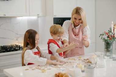 Mutlu anne ve çocuklar mutfak masasında kurabiye pişirirken kurabiye hamuruyla oynuyorlar..