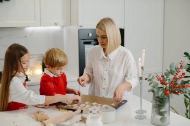 Çocuklu mutlu bir anne Noel kurabiyesi yapıyor ve onları mutfakta bir tepsiye koyuyor..