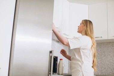 Genç kadın mutfaktaki buzdolabından bir galon süt alıyor..