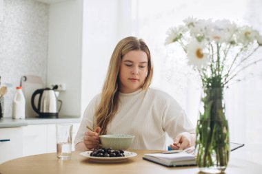 Sarışın kız elinde telefonla kahvaltı yapıyor..