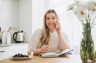 Evde genç ve güzel bir kız öğrenci, günlüğüne ya da defterine not alıyor, telefonla konuşuyor..
