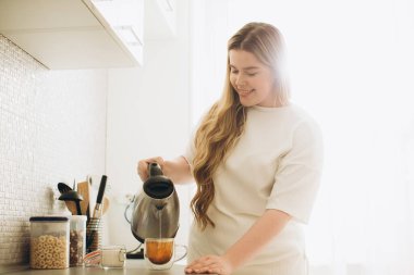 Gülümseyen genç bayan sabah mutfakta çay hazırlıyor..