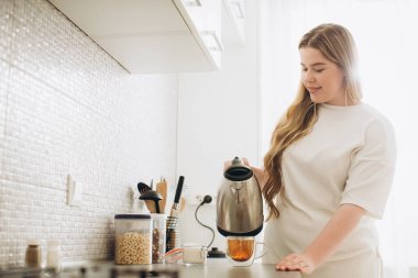 Gülümseyen genç bayan sabah mutfakta çay hazırlıyor..