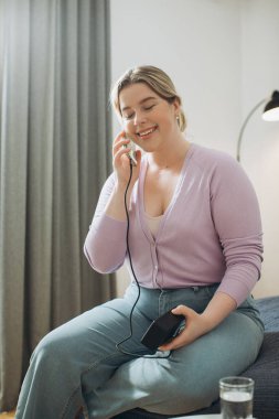 Evdeki yatakta otururken telefonu kullanan genç bir kadın..