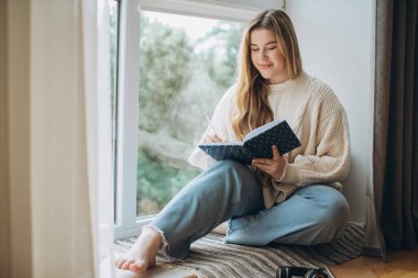 Yaratıcı genç kadın, evinde pencerenin yanında otururken hafıza planı ve fikir yazar. Yaratıcı günlük veya günlük kavramı.