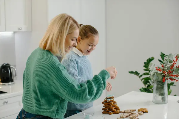 クリスマスの装飾と自宅で居心地の良いキッチンに立っている間に焼いた後 クリスマスジンジャーブレッドクッキーを飾る幸せな母とかわいい少女の娘 — ストック写真