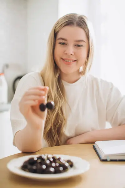 キッチンで自宅で熟したチェリーを食べる若い美しい少女 — ストック写真