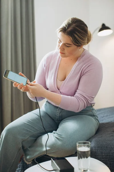 Young Woman Charging Her Phone Power Bank While Sitting Bed — Stock Photo, Image
