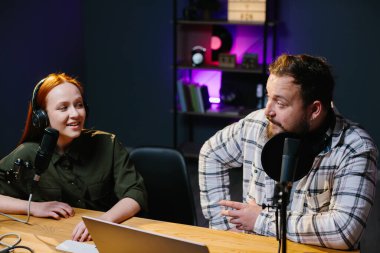 İki radyo sunucusu stüdyoda podcast yaparken gülüyor.