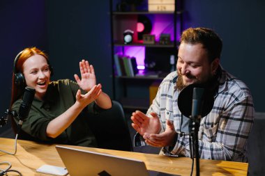 İki radyo sunucusu stüdyoda podcast yaparken gülüyor.