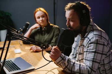 İki radyo sunucusu stüdyoda podcast yaparken gülüyor.