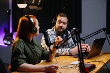 İki radyo sunucusu stüdyoda podcast yaparken gülüyor.